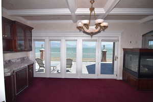 Dining room with a water and mountain view, plenty of natural light, dark colored carpet, coffered ceiling, and beamed ceiling
