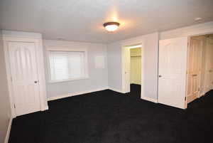 Unfurnished bedroom featuring a textured ceiling, dark colored carpet, and a spacious closet