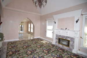 Unfurnished living room featuring a chandelier, arched walkways, a high end fireplace, and high vaulted ceiling