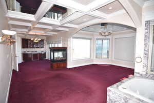 Unfurnished living room featuring a chandelier, coffered ceiling, beamed ceiling, dark colored carpet, and crown molding