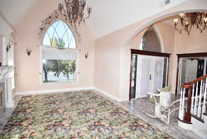 Entrance foyer with a chandelier, high vaulted ceiling, arched walkways, and light marble finish floors
