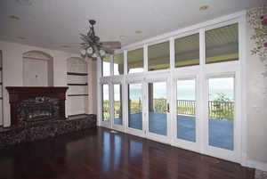Unfurnished living room featuring plenty of natural light, a fireplace, a water view, dark wood-type flooring, and a textured ceiling