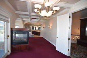 Corridor featuring a chandelier, coffered ceiling, beamed ceiling, dark carpet, and crown molding