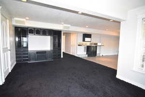 Unfurnished living room with a textured ceiling, dark carpet, and recessed lighting
