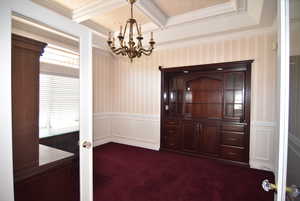 Unfurnished dining area featuring dark colored carpet, a decorative wall, a chandelier, ornamental molding, and a wainscoted wall
