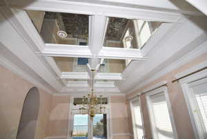 Detailed view of crown molding, coffered ceiling, a chandelier, and beam ceiling