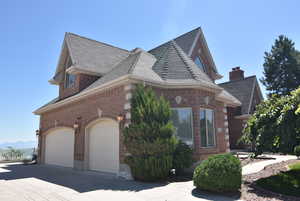 View of side of home featuring brick siding, a garage, driveway, and a shingled roof