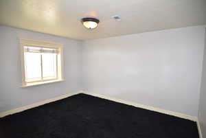 Carpeted empty room with a textured ceiling and baseboards
