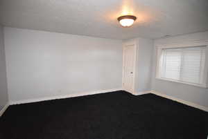 Empty room featuring dark carpet and a textured ceiling