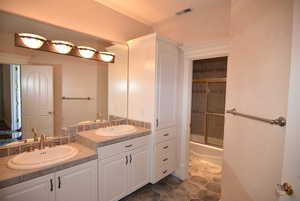 Full bath with combined bath / shower with glass door and dark tile patterned flooring