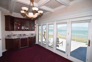 Bar with a water view, dark colored carpet, light countertops, glass insert cabinets, and dark brown cabinetry