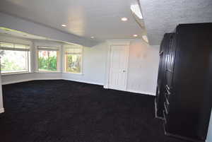 Empty room featuring dark carpet, a textured ceiling, and recessed lighting