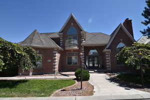 View of front of house featuring a balcony, brick siding, french doors, a chimney, and roof with shingles