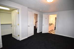 Unfurnished bedroom featuring a textured ceiling, dark carpet, and ensuite bathroom
