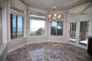 Unfurnished dining area with a water view, a chandelier, dark marble finish floors, and recessed lighting
