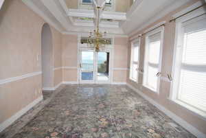 Unfurnished dining area featuring arched walkways, ornamental molding, a chandelier, coffered ceiling, and beam ceiling