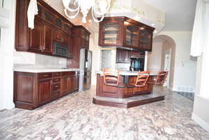 Kitchen with backsplash, arched walkways, black appliances, a chandelier, and dark brown cabinetry
