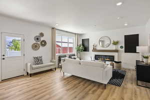Living area with light wood finished floors, a glass covered fireplace, and recessed lighting