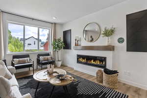 Living area featuring light wood-style floors, a glass covered fireplace, and recessed lighting