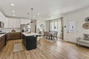 Kitchen featuring a kitchen bar, hanging light fixtures, stainless steel appliances, a kitchen island with sink, and white cabinets