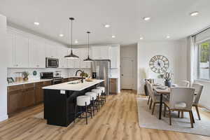 Kitchen with stainless steel appliances, an island with sink, pendant lighting, a kitchen breakfast bar, and light wood-style floors