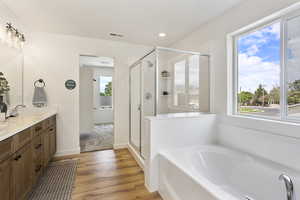 Full bath with double vanity, a garden tub, a shower stall, light wood-style flooring, and recessed lighting