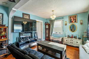Living room with a chandelier, wood finished floors, and a textured ceiling