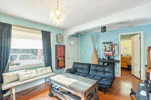 Living area with hardwood / wood-style flooring, arched walkways, a textured ceiling, and a chandelier