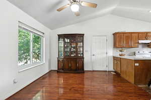 Kitchen with light countertops, dark wood finished floors, lofted ceiling, white electric range, and brown cabinets