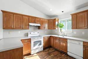 Kitchen with brown cabinets, white appliances, lofted ceiling, light countertops, and under cabinet range hood