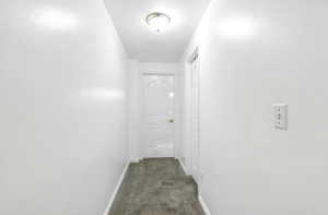 Hall featuring dark colored carpet and baseboards