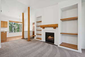 Unfurnished living room with carpet flooring, a chandelier, built in features, a fireplace with flush hearth, and lofted ceiling