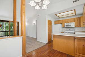 Kitchen with dark wood-type flooring, light countertops, white appliances, a peninsula, and lofted ceiling