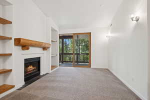 Unfurnished living room with carpet flooring, a fireplace with flush hearth, and built in shelves