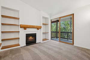 Unfurnished living room with carpet floors, built in features, and a fireplace with flush hearth