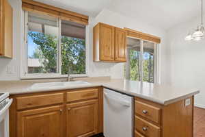 Kitchen with dishwasher, a peninsula, light countertops, brown cabinets, and a chandelier