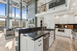 Kitchen featuring stainless steel appliances, a fireplace, white cabinetry, backsplash, and a kitchen island with sink