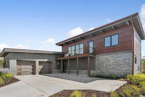 View of front of house with stone siding, a balcony, an attached garage, and driveway