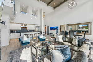 Living room featuring beam ceiling, a chandelier, wood finish floors, a towering ceiling, and recessed lighting