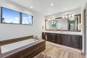 Full bath with double vanity, a garden tub, recessed lighting, and wood finished floors