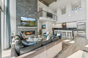 Living area featuring wood tiled floors, a stone fireplace, beamed ceiling, a high ceiling, and recessed lighting