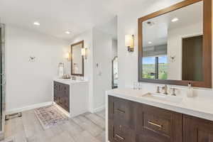 Bathroom with two vanities, recessed lighting, and wood finished floors