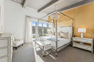Carpeted bedroom with access to outside, beam ceiling, and a chandelier