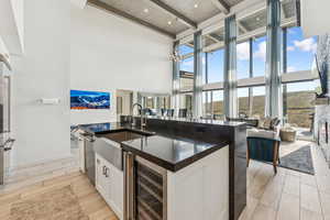 Kitchen with wood tiled floors, a high ceiling, beam ceiling, wine cooler, and white cabinetry