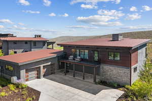 View of front facade featuring stone siding, a metal roof, driveway, a mountain view, and an attached garage