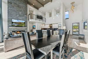 Dining area with wood finish floors, a stone fireplace, beam ceiling, a towering ceiling, and recessed lighting