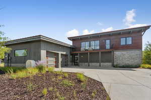 Back of house with stone siding, a balcony, an attached garage, and driveway