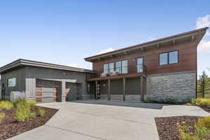 View of front of property with stone siding, a balcony, a garage, and driveway