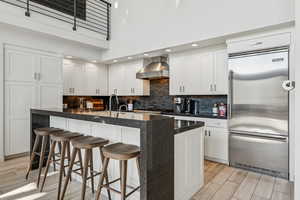 Kitchen with built in fridge, wood tiled floors, a high ceiling, decorative backsplash, and wall chimney range hood