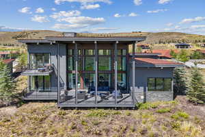 Rear view of property with a mountain view, stone siding, a balcony, and a sunroom